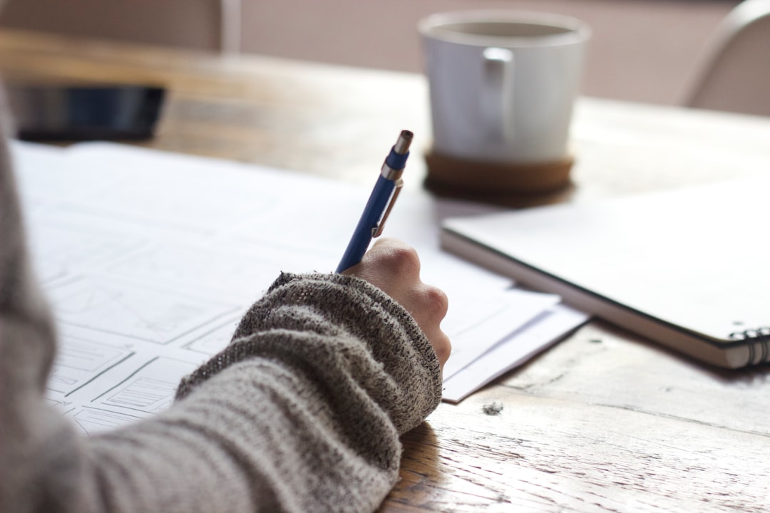 Photo by Unseen Studio person writing on brown wooden table near white ceramic mug
